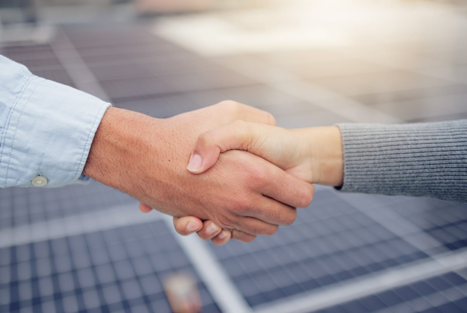 Business partners shaking hands with solar panels in the background